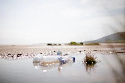 A Couple of Empty Plastic Bottles on a Puddle in the Middle of the Sand Stock Photos