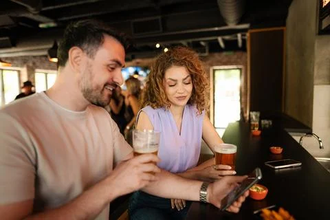 Couple enjoying drinks and using smartphone in pub Stock Photos