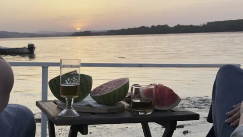 Couple Enjoying Drinks and Watermelon by River at Sunset Stock Footage 334571553