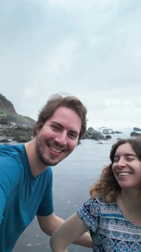 Couple enjoying laughter while taking playful selfies on a rocky beach Stock Footage 294276238