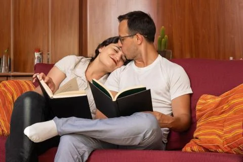 Couple enjoying romantic time at home reading and kissing on the sofa Stock Photos