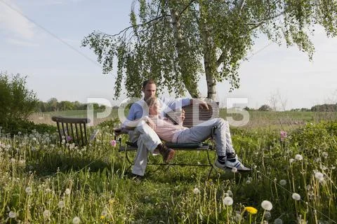A couple enjoying sunshine and wine on a bench in their backyard Stock Photos