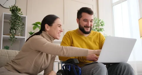 Couple enjoying using laptop with man on wheelchair Stockbeeldmateriaal 145219797