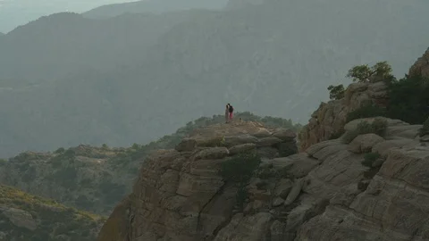 A couple enjoying the view from on top of a cliff in the mountains Stock Footage 112950603