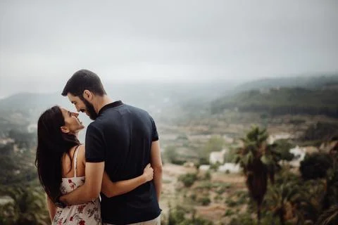 Couple enjoying view while standing on hill and hugging Stock Photos