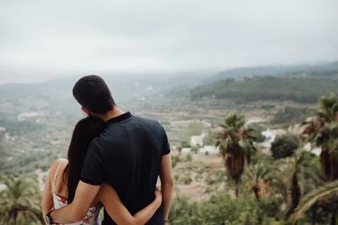 Couple enjoying view while standing on hill and hugging Stock Photos