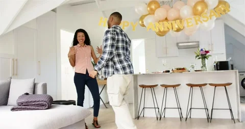 Couple entering loft draping throw arranging cake and glasses under anniversary 스톡 동영상 317064770