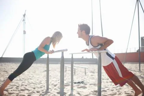 Couple exercising on beach, stretching, using gymnastics parallel bars Stock Photos