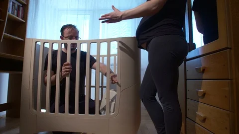 Couple expecting baby assembling baby bed in newly decorated room Stock Footage 89460892