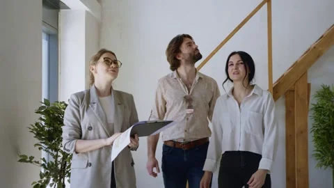 Couple Exploring Flat with Realtor Showing Plans and Layout Stockbeeldmateriaal 311855057