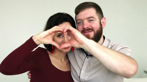 Couple faces look through joined fingers making heart shape Stock Footage 180406600