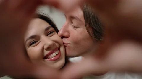 Couple faces looking through joined fingers making heart shape Stock Footage 234619313