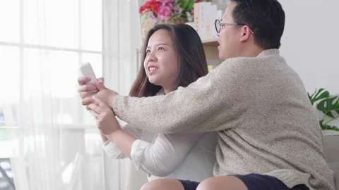 Couple fighting for remote control while watching TV on sofa in living room Video stock 163773041