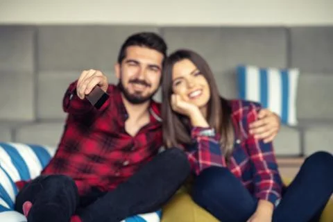 Couple fighting for remote control while watching TV at home Stock Photos