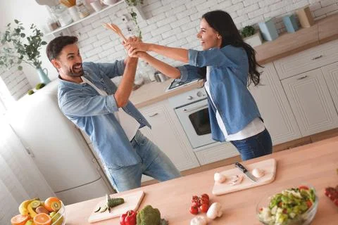 Couple fighting on spatulas in the kitchen while preparing dinner Stock Photos