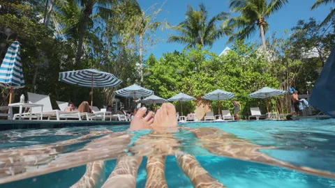 Couple floating in tropical resort pool with feet above water and palm trees. Vídeo Stock 339802358