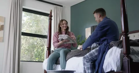 Couple folding laundry on four-post bed passing garments into basket prompted by Stock Footage 348445889