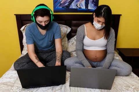 Couple of future young parents using laptops to work at home and to play onli Stock Photos