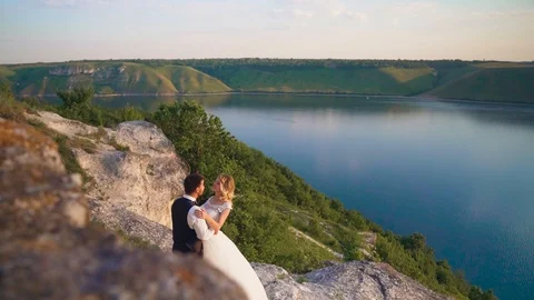 Couple gently embrace standing on the edge of the cliff and looking on the lake Video stock 107809376