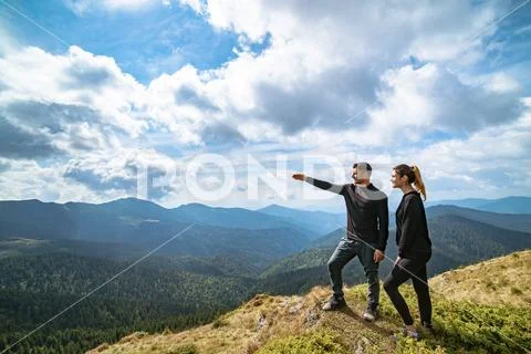The couple gesturing on the mountain with a picturesque cloudscape Stock Photos