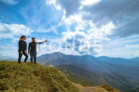 The couple gesturing on the mountain with a picturesque cloudscape Stock Photos
