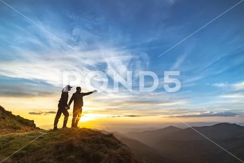 The couple gesturing on the mountain with a picturesque sunset Stock Photos