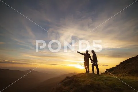 The couple gesturing on the rock with a picturesque sunset Stock Photos