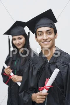 Couple in graduation gowns holding diplomas and smiling Stock Photos