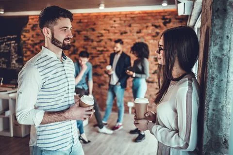 Couple of happy colleagues talking while standing at the office brick wall wi Stock Photos