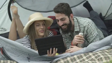 Couple has a good time at camping trip, using a digital tablet in the tent Video stock 74733995
