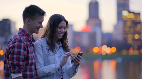 Couple Have Fun Looking Through Photos On Their Phone, City In Background Stock Footage 61042753