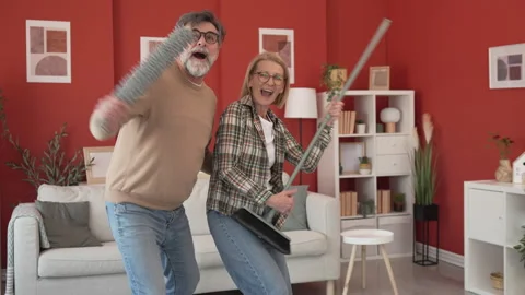Couple have fun while clean living room use broom like electric guitar Stock Footage 303993233