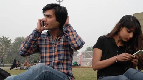Couple having an argument in a public park over phone calls on a mobile phone Stock Footage 59506970