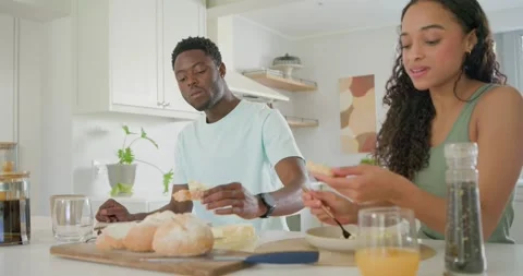 Couple having breakfast at kitchen island man blue tee holding bread woman green Stock Footage 337225169