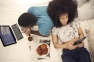 Couple Having Croissants And Using Technology While Resting On Bed At Home Stock Photos