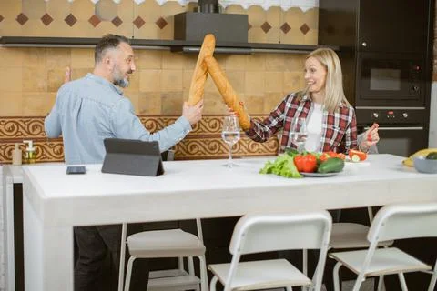 Couple having fun on kitchen while fighting with baguettes 스톡 사진