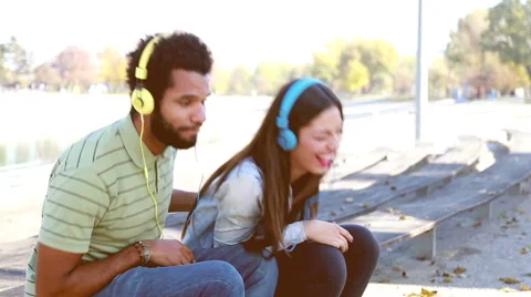 Couple having fun listening to music on headphones at the park Stock Footage 59555020