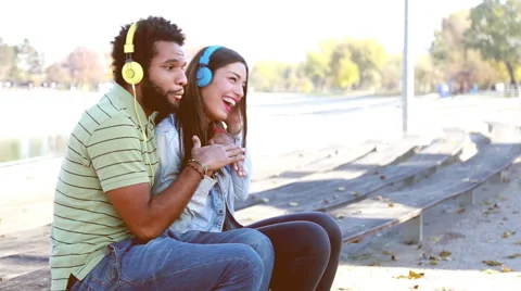 Couple having fun listening to music on headphones at the park Stock Footage 59555025