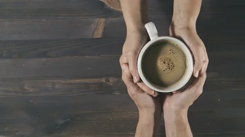 Couple holding cup of coffee in hands on wooden background, top view Stock Footage 81443861