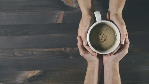 Couple holding cup of steaming coffee in hands on wooden background Stock Footage 81443787