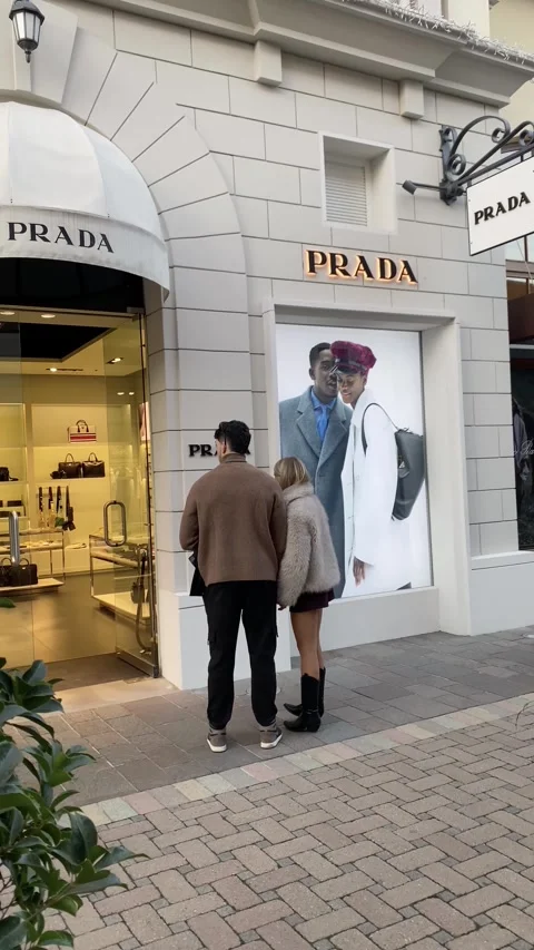 Couple holding hands looking Prada shop window at Fidenza Village shopping Stock Footage 297347577