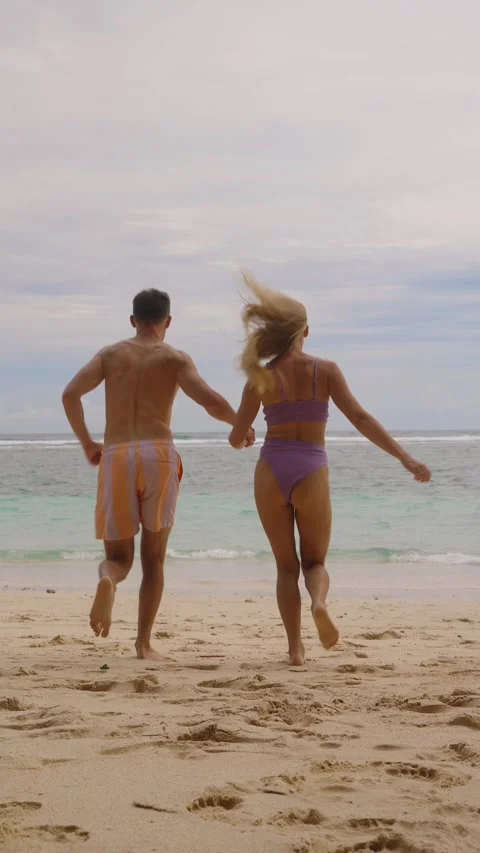 Couple holding hands running on sandy beach toward ocean Stock Footage 296489166