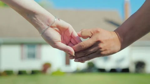 Couple holding hands slowly in front of blurred house exterior on sunny day. Stockbeeldmateriaal 334705510