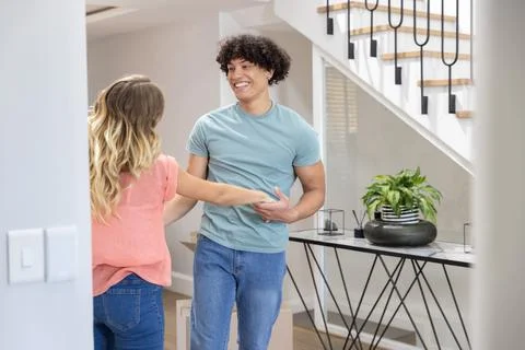 Couple holding hands, smiling while unpacking boxes near console table and Stock Photos