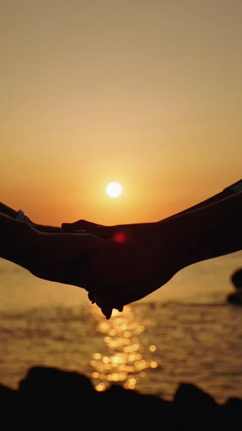 Couple holding hands at sunset over ocean with sun reflection on water. Vídeo Stock 334902004
