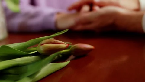 Couple holding hands with tulips on a table, showing love and companionship.. Stock Footage 297891227