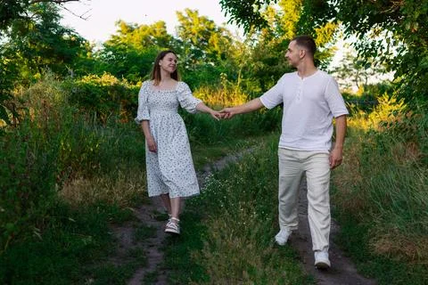 Couple holding hands walking on a path through a lush green summer meadow Foto stock