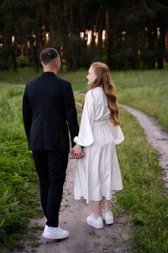 Couple holding hands walking on a path through a forest at sunset Foto stock