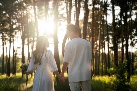 Couple holding hands walking through a sunlit forest during golden hour Stock Photos