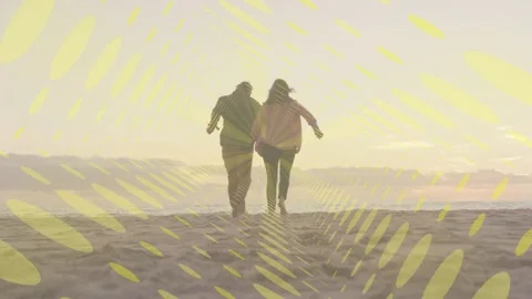 Couple holding hands walking toward sea at sunset spurring jogs, yellow overlay Video stock 333414046